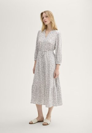 Robe midi blanche avec un décolleté en V, taille froncée et manches longues. Présente un motif texturé gris, accompagnée de sandales plates.