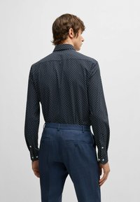 Granatowa koszula z długim rękawem w białe wzory w diamenty, z zapięciem na guziki przy mankietach i usztywnionym kołnierzykiem, w zestawie z ciemnoniebieskimi spodniami o dopasowanym kroju.