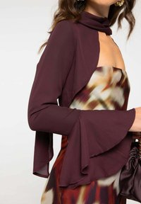 Chaqueta de chiffon burdeos con un cuello alto y mangas acampanadas, combinada con un vestido de satén multicolor con patrones abstractos.