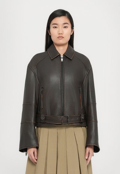 Brown leather cropped jacket with a high collar, front zipper, side pockets, and a belted waist. Features wide sleeves and contrast stitching.
