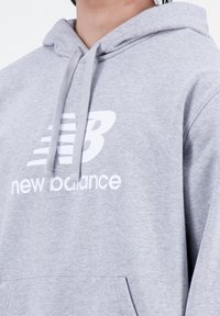 Felpa grigia realizzata in tessuto misto cotone, con logo stampato bianco e cappuccio con cordino. Include una tasca frontale.