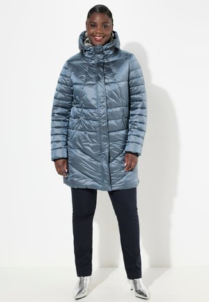 Lichtblauwe quilted pufferjas met capuchon, ritssluiting aan de voorkant en lange mouwen. Gecombineerd met zwarte broek en zilveren enkellaarsjes.