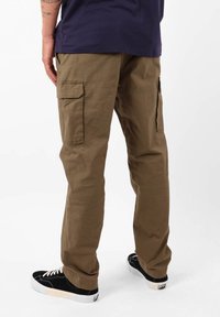 Pantalons cargo en vert olive avec une coupe décontractée, dotés de poches latérales et de détails de couture. Associés à des baskets noires.