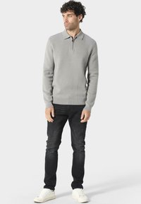 Grå langermet polo genser med glidelåskrage, kombinert med sorte jeans og hvite joggesko. Mykt stoff og tettsittende design.