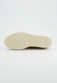 Semelle de chaussure couleur blanc cassé avec une texture antidérapante et un logo discret. Bords supérieurs marron avec une finition lisse. Forme arrondie avec une légère cambrure.