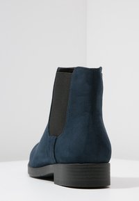 Bottines en cuir suédé bleu marine avec des panneaux latéraux élastiques, un petit talon empilé et une texture lisse. Présente un design à bout arrondi.