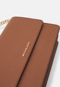 Brązowy skórzany portfel z złotym logo "Michael Kors" i złotym łańcuszkowym paskiem, pokazany na białym tle.