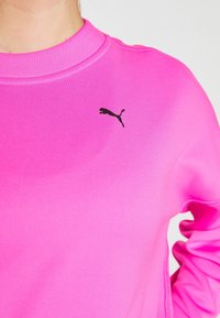 Felpa fucsia a maniche lunghe con scollo a girocollo e logo Puma nero sul lato sinistro del petto. Tessuto morbido con polsini a coste.
