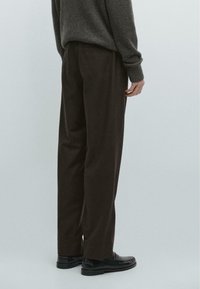 Ciemnobrązowe wełniane spodnie o luźnym kroju, z bocznymi kieszeniami i gładką teksturą, w połączeniu z czarnymi mokasynami.