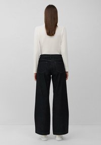 Jean en denim noir à jambes larges avec une taille haute, présentant des poches arrière et un ourlet net. Associé à un haut à manches longues côtelé blanc.