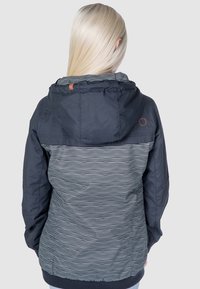Krycí bunda v tmavě námořnické barvě, se pruhovaným vzorem na dolní části. Materiál vypadá lehký, s texturovaným povrchem a elastickými manžetami.
