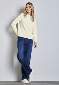 Hellgelber, gesteppter Pullover mit Rundhalsausschnitt, kombiniert mit dunkelblauen, weiten Jeans und weißen Sneakern, präsentiert ein lässiges Design.