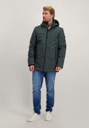 Dark green jacket with a hood, zip closure, and side pockets. Worn with blue jeans and white sneakers, set against a light background.