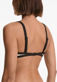 Reggiseno nero con spalline larghe, caratterizzato da un design incrociato sul retro e hardware regolabile. Tessuto liscio con un aspetto minimalista.
