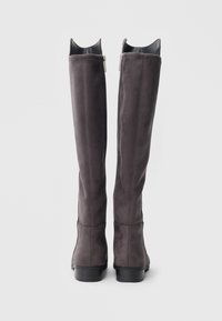 Grå overkne-st�øvler i semsket skinn med tettsittende form, glidelåslukking bak og lav stablet hæl. Merkbare utskjæringsdetaljer øverst.