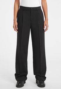Pantaloni a gamba larga neri con vita alta, dotati di pieghe frontali, tasche laterali e chiusura con bottone. Realizzati in un tessuto liscio e intrecciato.