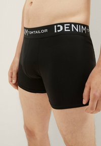 Fekete boxer alsónadrág puha gumis derekú, ami "DENIM TOM TAILOR" felirattal van ellátva fehér színben. Sima textúrájú, testhezálló szabás, térd hosszúságú.