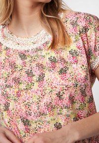 Blusa con estampado floral en rosa, amarillo y verde. Presenta un escote redondo con detalles de encaje. Tejido suave con mangas cortas.