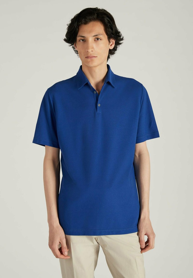 Camiseta polo azul hecha de tela suave, con mangas cortas, un collar con dos botones y un corte relajado. Diseño simple y clásico.