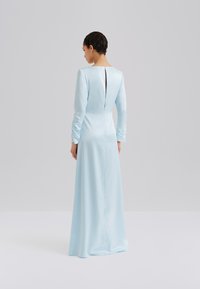 Φόρεμα από σατέν σε ανοιχτό μπλε χρώμα με μακριά μανίκια, που διαθέτει σκίσιμο στο πίσω μέρος και διακριτικό σούρωμα στα μανίκια, με στρογγυλή λαιμόκοψη και εφαρμοστή σιλουέτα.