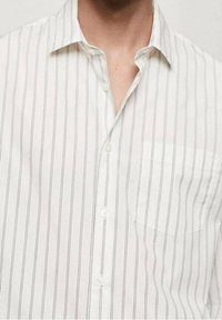 Chemise blanche à fines rayures verticales noires, boutonnée sauf le premier bouton en haut, dotée d'une poche poitrine gauche.