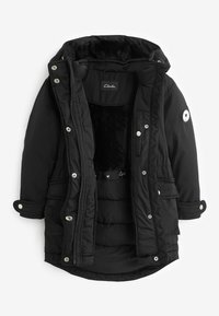 Čierna puffa bunda s kožušinovou podšívkou, cvokmi, nastaviteľnými manžetami a kapucňou. Na rukáve má nášivku s logom Clarks.