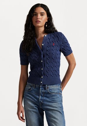 Mörkblå kabelstickad cardigan med korta ärmar, med knäppning framtill, ribbad fåll och en liten röd logotyp på vänster bröst.