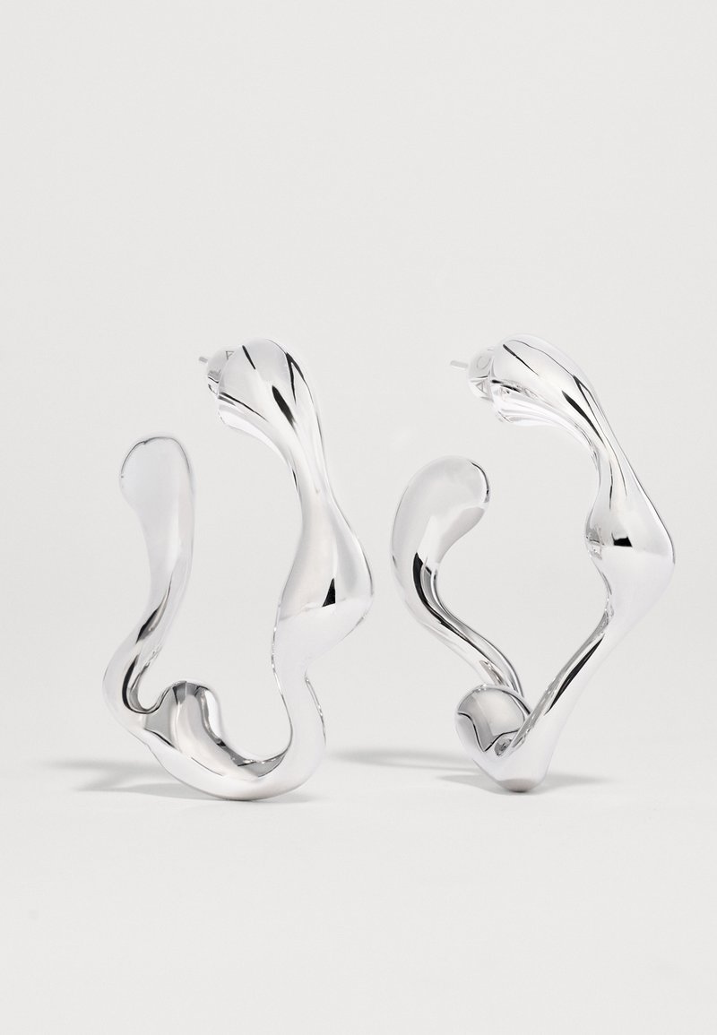 Ασημένια σκουλαρίκια κρίκοι με κυματιστό, αφηρημένο σχέδιο, λεία, αντανακλαστική επιφάνεια και ακανόνιστες οργανικές μορφές.