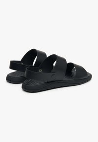 Czarne sandały wykonane z materiału syntetycznego z dwoma szerokimi paskami i teksturowaną wkładką. Charakteryzują się płaską podeszwą i regulowanym elementem wykończenia.