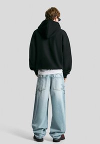 Black oversized hoodie with a drawstring hood, paired with light blue baggy jeans featuring contrasting stitching and wide legs.