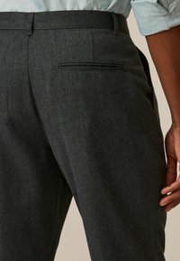 Pantalons taillés gris avec une texture lisse, dotés d'une poche arrière unique et d'une coupe droite. Tissu doux, lignes épurées.