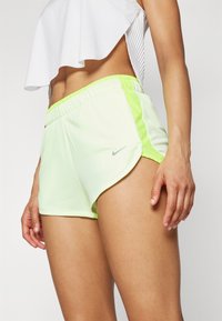 Shorts de sport légers, de couleur vert néon, avec une texture en maille, dotés d'une taille élastique et d'un logo Nike argenté sur le côté.
