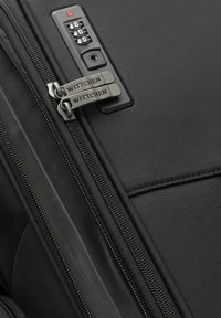 Czarny bagaż o teksturowanej powierzchni, wyposażony w podwójne metalowe zamki błyskawiczne, zamknięcie szyfrowe oraz grawerunek marki na suwakach.
