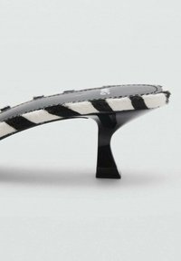 Sandalo con tacco a strisce bianche e nere dal profilo elegante e curvato, con tacco nero lucido e tomaia in un materiale testurizzato simile alla pelliccia.