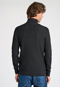 Pullover nero in maglia con un motivo a diamante testurizzato, colletto alto e polsini a costine. Indossato con jeans in denim blu, mostrando una vista posteriore casual.