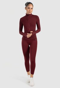 Dunkelrotes Sportset mit enganliegender Jacke mit Reißverschluss und hohem Kragen sowie passenden Leggings. Hergestellt aus glattem, elastischem Material.