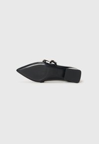 Chaussure noire à bout pointu avec un petit talon carré, doubles brides à la cheville et détails de boucles dorées, vue du côté de la semelle.