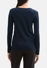 Pull long bleu marine à manches longues avec un col rond, texture côtelée et coupe ajustée. Détails de couture le long des épaules et des manches.