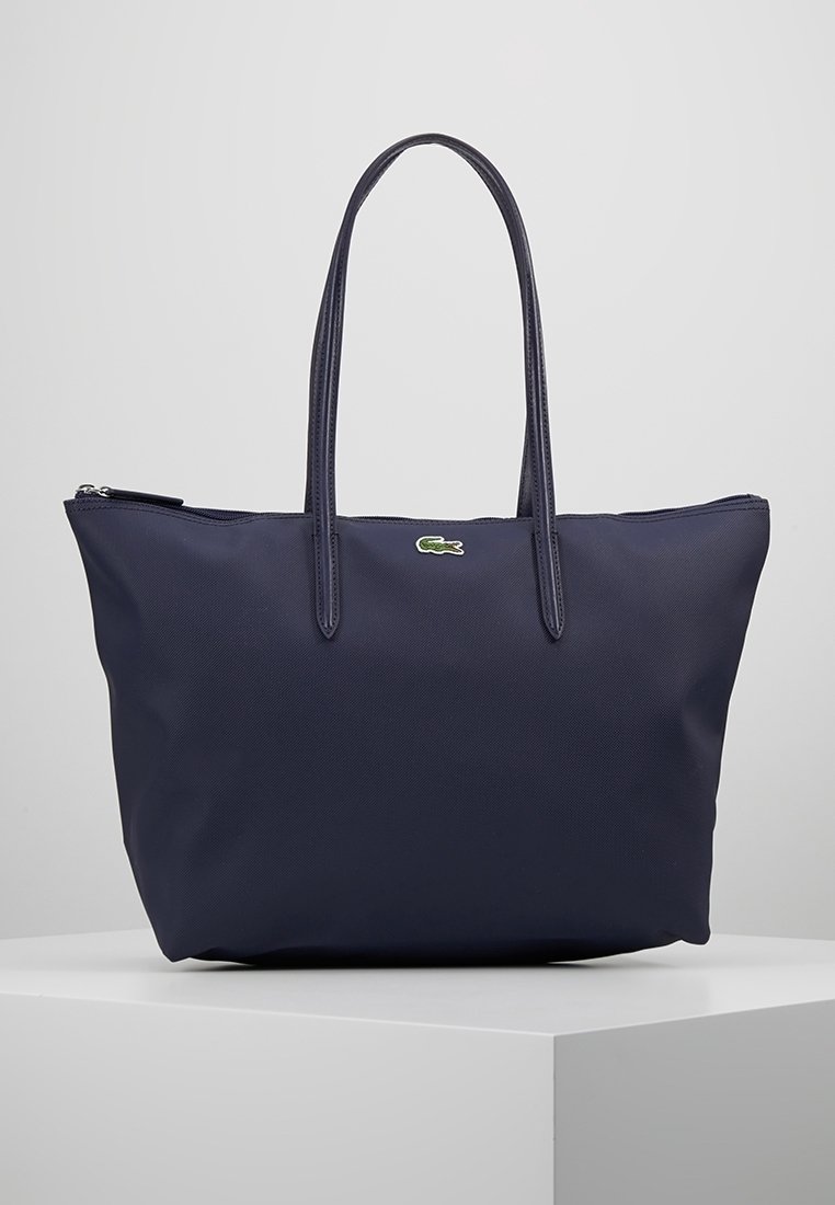 Sac fourre-tout bleu marine en tissu texturé avec deux longues anses, fermeture éclair et un petit logo vert en accent.
