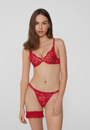 Conjunto de lencería de encaje rojo que incluye un bralette con aros, tirantes ajustables y un tanga a juego con acentos fruncidos en el liguero.
