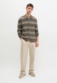 Gebreid vest met horizontale strepen in bruin en beige, knoopsluiting aan de voorkant, en een kraag. Gecombineerd met beige broek en beige schoenen.