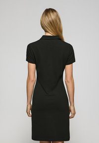 Czarna sukienka polo z krótkimi rękawami, kołnierzykiem i prostym dołem. Gładka tekstura, dopasowany krój i sięgająca powyżej kolana z tyłu.