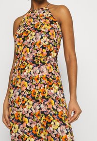 Vestido sin mangas con estampado floral que presenta un fondo negro con flores rosas, naranjas y amarillas. Diseño de cuello halter, la tela cae suavemente.