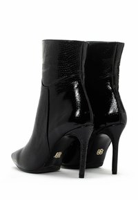 Ein Paar schwarze, hochhackige Stiefeletten mit strukturiertem, glänzendem Material und spitzen Zehen, von hinten auf einem weißen Hintergrund gezeigt.