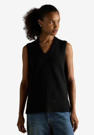 Top de punto negro sin mangas con escote en V, que presenta una textura acanalada en el dobladillo. Combinado con unos vaqueros de denim azul claro.