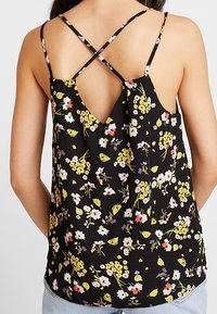Top senza maniche nero a fiori con spalline incrociate, decorato con piccoli fiori gialli, rosa e bianchi sparsi sul tessuto.