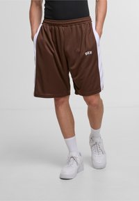 Shorts de sport marron avec panneaux latéraux blancs, taille élastique et poches. Présente l'inscription "DEF" en lettres blanches sur le devant. Associés à des baskets blanches.