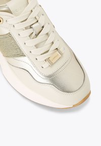 Kremowe skórzane sneakersy z metalicznymi akcentami, teksturowaną wstawką i beżowymi sznurówkami, z złotym detalem logo po boku.