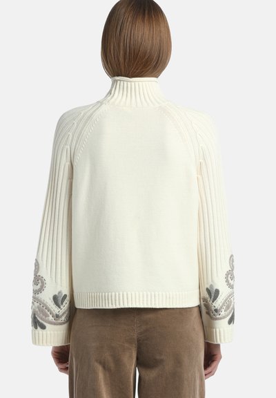 Maglione lavorato a maglia di colore crema con colletto alto, maniche a coste e complessi ricami floreali grigi ai polsini. Texture liscia.