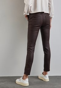 Bruna slim-fit jeans med en slät yta, femficksdesign och subtila sömnadsdetaljer, i kombination med vita sneakers.